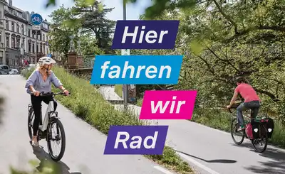 Radfahrende auf einem Radweg in städtischer Umgebung mit Texteinblendung Hier fahren wir Rad