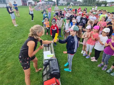 Staffelstabübergabe bei Schulveranstaltung auf Sportplatz mit Schülern und betreuenden Lehrkräften