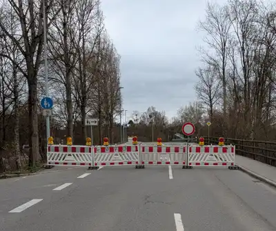 Straßensperrung mit Absperrbarieren und Warnleuchten blockiert Zufahrt zu Brücke, Verkehrszeichen weist auf Fußgängerumleitung hin